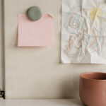 affirmations-for-tired-moms-featured A blank pink note held by a sage magnet on a cream fridge beside a crayon drawing, with a terracotta mug below