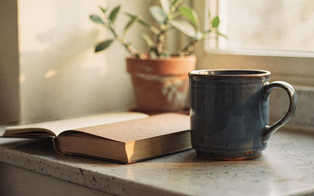 How to Feel Like Yourself Again as a Mom, a Few Minutes at a Time A blue mug and an open book on a sunny windowsill beside a potted plant