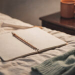 five-minute-journal-prompts-for-moms-featured An open blank notebook with a pencil on a cream bed beside a sage cardigan and a terracotta mug