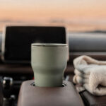 self-care-for-moms-with-no-time-featured A sage travel mug in a parked car cup holder beside a folded cream cardigan at golden hour
