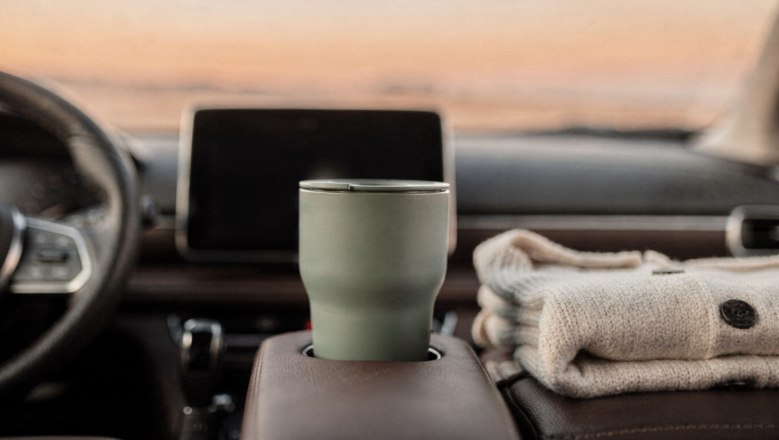 self-care-for-moms-with-no-time-featured A sage travel mug in a parked car cup holder beside a folded cream cardigan at golden hour