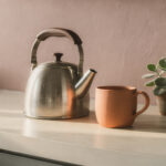 small-daily-self-care-ritual-featured A kettle, a terracotta mug and a small green plant on a cream counter in morning light