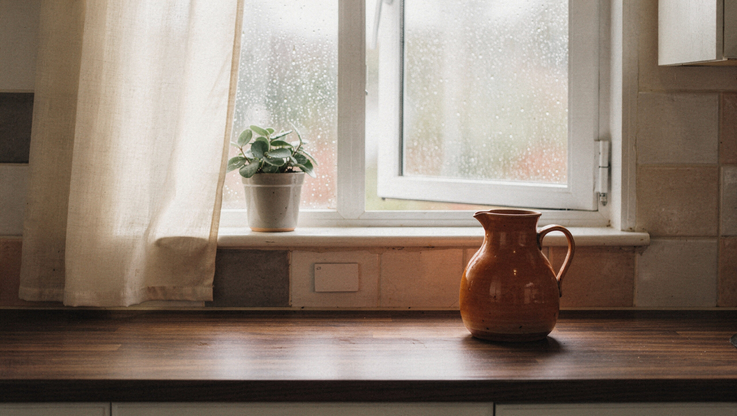 stuck-inside-with-kids-open-a-window-featured A kitchen window open to a rainy day, a sheer cream curtain, a small plant on the sill and a terracotta jug